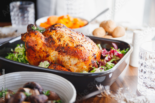 Whole roasted chicken served with fresh salad in black pan on a festive table. Thanksgiving or family dinner celebration cooking concept.