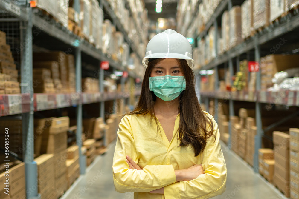 Female warehouse worker inspecting a warehouse in a factory. Wear a safety helmet and mask for working safety. Concept of warehouse.