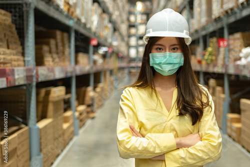 Female warehouse worker inspecting a warehouse in a factory. Wear a safety helmet and mask for working safety. Concept of warehouse.