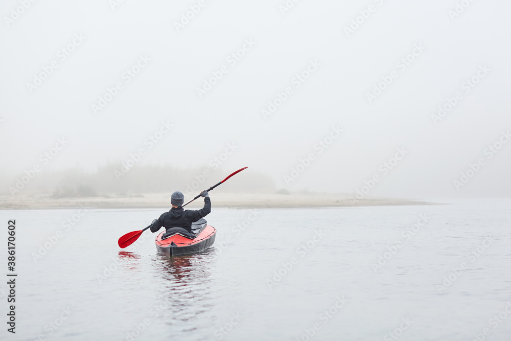 Naklejka premium Kayaker rowing boat to bank of river, holding paddle in hands. wearing warm clothing, sportsman posing backwards in canoe, water sport, extreme.