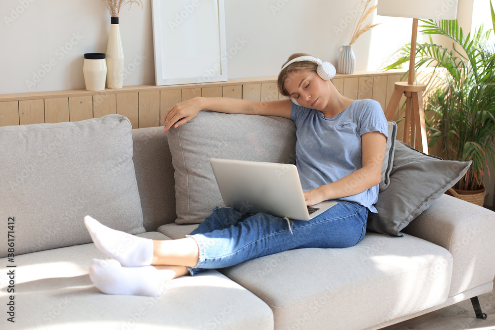 Smiling young woman with headphones and laptop on the sofa. Smiling young woman with headphones and laptop on the sofa.
