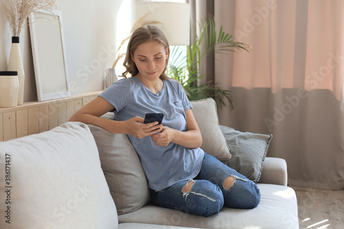 Pretty girl using her smartphone on couch at home in the living room.