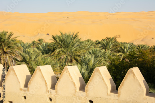Palm trees and the sand dunes of Liwa Oasis in the Empty Quarter (Rub' al Khali) part of the larger Arabian Desert in the United Arab Emirates, seen through the walls of an old Arabian style fort photo