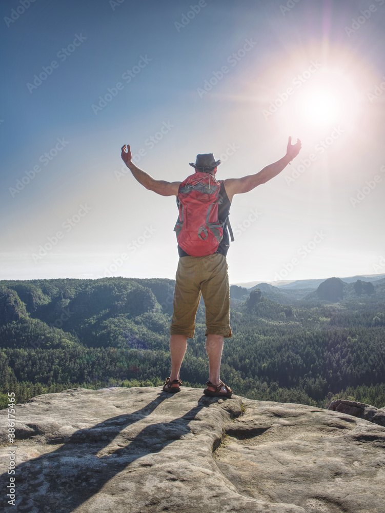 Obraz premium Happy hiker with red backpack raised hands on rock
