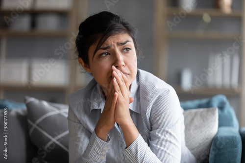 Sad indian woman feels miserable desperate sit on sofa look out the window thinking about personal troubles does not see way out of difficult life situation. Break up, heartbreak, cheated girl concept
