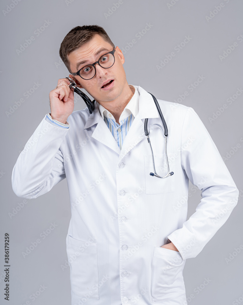 Young handsome doctor in scrubs put phonendoscope to ear. Funny emotions. Young handsome doctor in scrubs put phonendoscope to ear. Funny emotions.