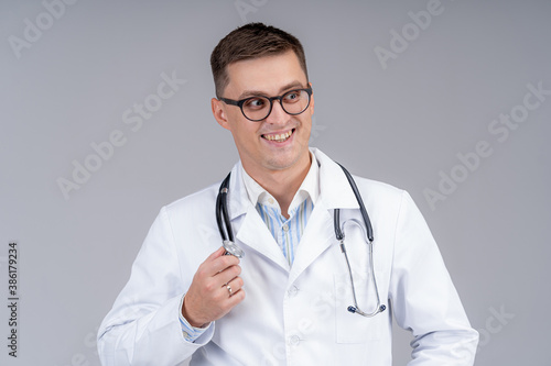Portrait of doctor in scrubs. Gray background. Smiling doctor in glasses with phonendoscope. Close up shot. © Vadim