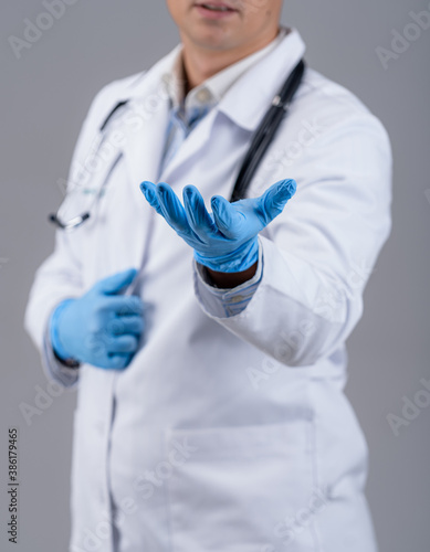 Doctor is showing one hand in blue medical gloves to the camera. Medic in white scrubs with phonendoscope. Cropped photo. Closeup.