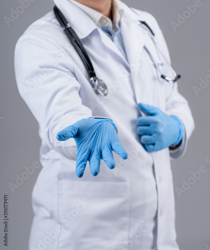 Medic in blue latex gloves shows hands to the camera. Doctos in white scrubs with stethoscope on neck. Studio photo with selective focus.
