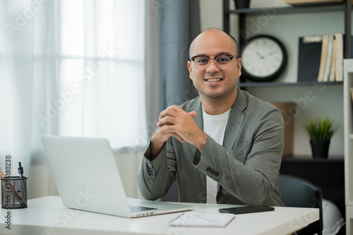 A middle-aged man around the age of 35. Working at home Work through the laptop by meeting video conference. He was wearing a grey suit and glasses. Smiling asian businessman work from home.