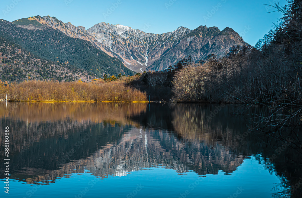 Landscape photo of Japan Alps with snow on top of the mountain in autumn at Kamikochi, Japan. There is an emerald blue lake with reflection in the water. Idea for autumn background with copy space.