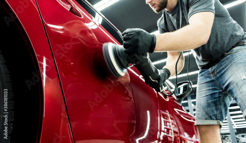 Car service worker polishes a car details with orbital polisher.