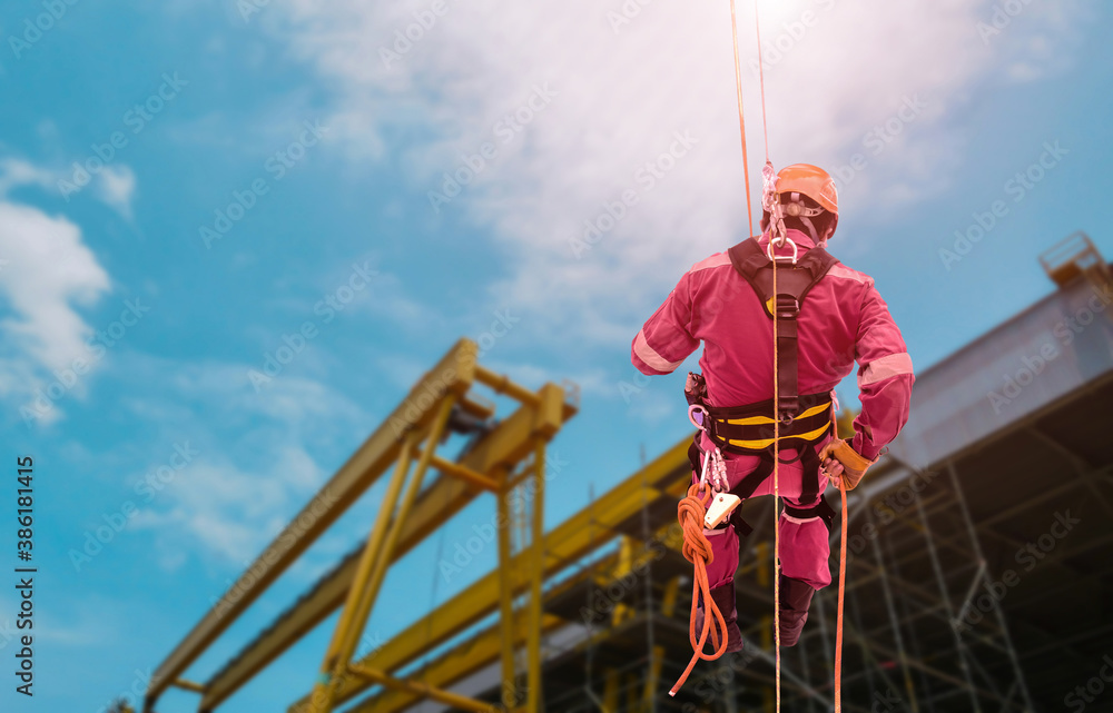 Worker Abseiling from high places Closeup pic of male rope access jobs worker wearing white hard hat, long sleeve shirt, safety harness, working at height abseiling down from the high rise. Worker Abseiling from high places Closeup pic of male rope access jobs worker wearing white hard hat, long sleeve shirt, safety harness, working at height abseiling down from the high rise.