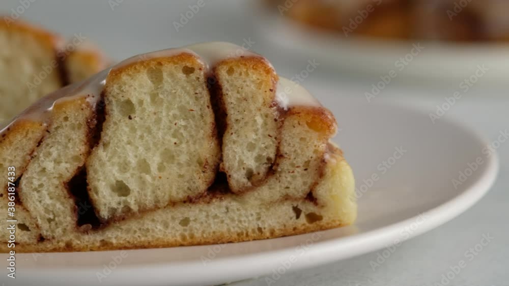 Close-up cut of cinnamon rolls on a plate. Sweet cream cheese frosting pouring on cinnamon rolls. Production of cinnamon rolls. Bakery products. Appetizing cinnamon buns Close-up cut of cinnamon rolls on a plate. Sweet cream cheese frosting pouring on cinnamon rolls. Production of cinnamon rolls. Bakery products. Appetizing cinnamon buns