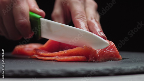 Sushi Chef Slices fresh Salmon on the sushi bar. Chef cutting salmon fillet at professional kitchen. Closeup chef hands slicing fresh fish slice in slow motion. Professional man cutting red fish