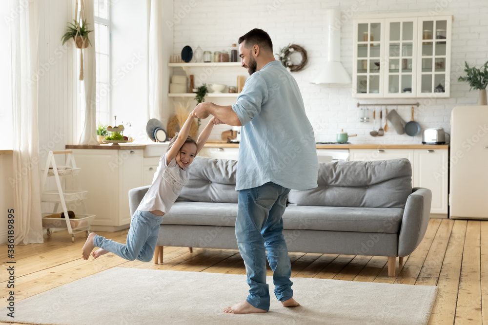Happy young father spinning little daughter, holding hands, family playing funny active game at home, overjoyed dad and laughing cute preschool girl having fun in modern living room together Happy young father spinning little daughter, holding hands, family playing funny active game at home, overjoyed dad and laughing cute preschool girl having fun in modern living room together