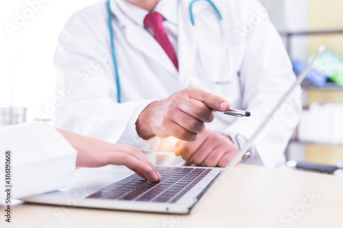 Unrecognizable doctor working with team on laptop computer in doctor   s office. Professional doctor reading result of medical test of patient. Doctors diagnose symptom on notebook computer together