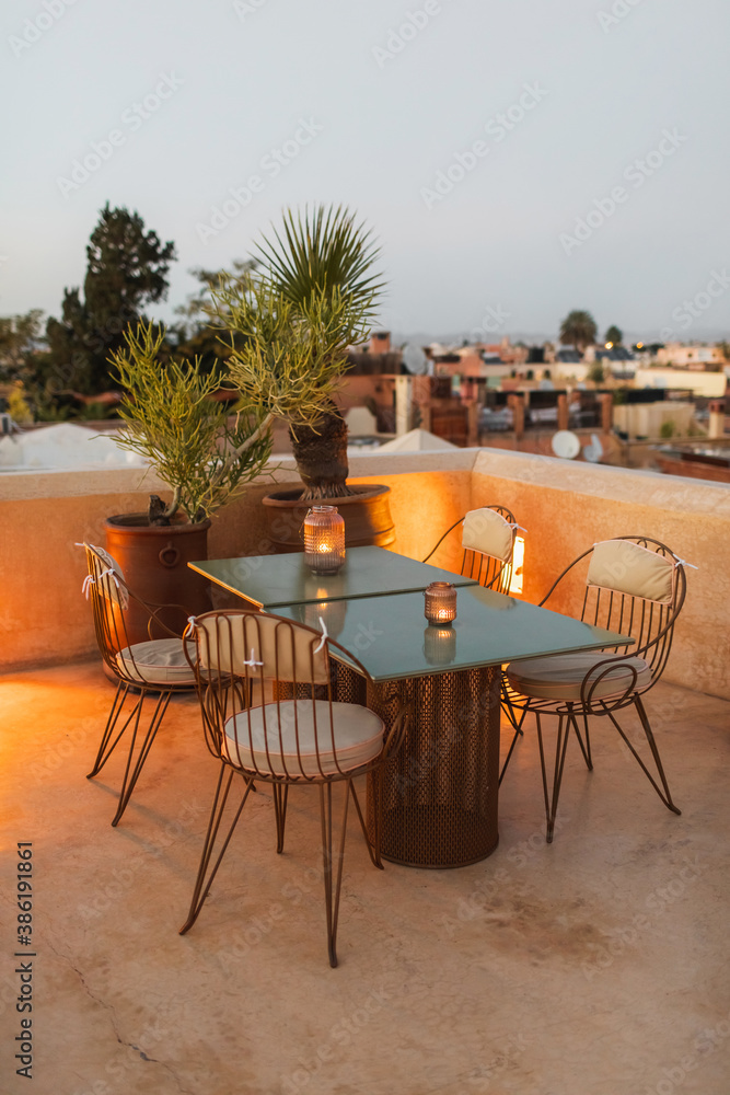 Table for romantic dinner on rooftop terrace in evening. Moroccan style, vintage lamps, candles, cactus flower, twilight.
