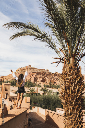 Happy woman enjoying famous moroccan landmark ksar Ait-Ben-Haddou. View from behind. Travel in Morocco, Ouarzazate. Wanderlust concept.