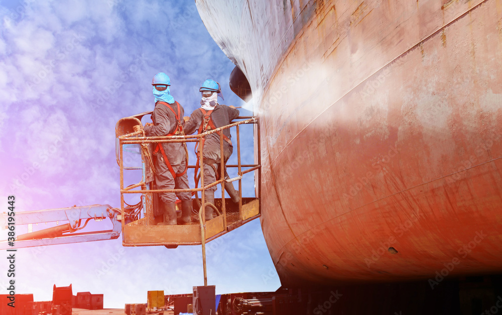 Worker wearing safety harness cleaning washing wall shell ship at high