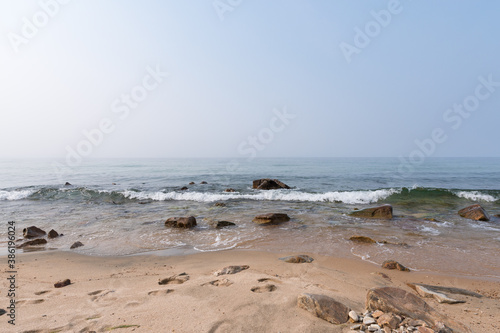 Eastern shore of Lake Baikal on a foggy day. Waves roll over the stones and wash the tracks off the sand