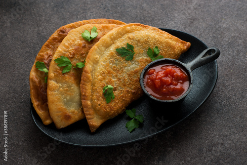 Homemade chebureks with filling and tomato sauce on a dark background photo