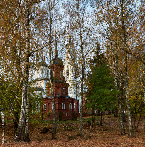 An old Russian church at dawn peeping through birches with bright autumn leaves.