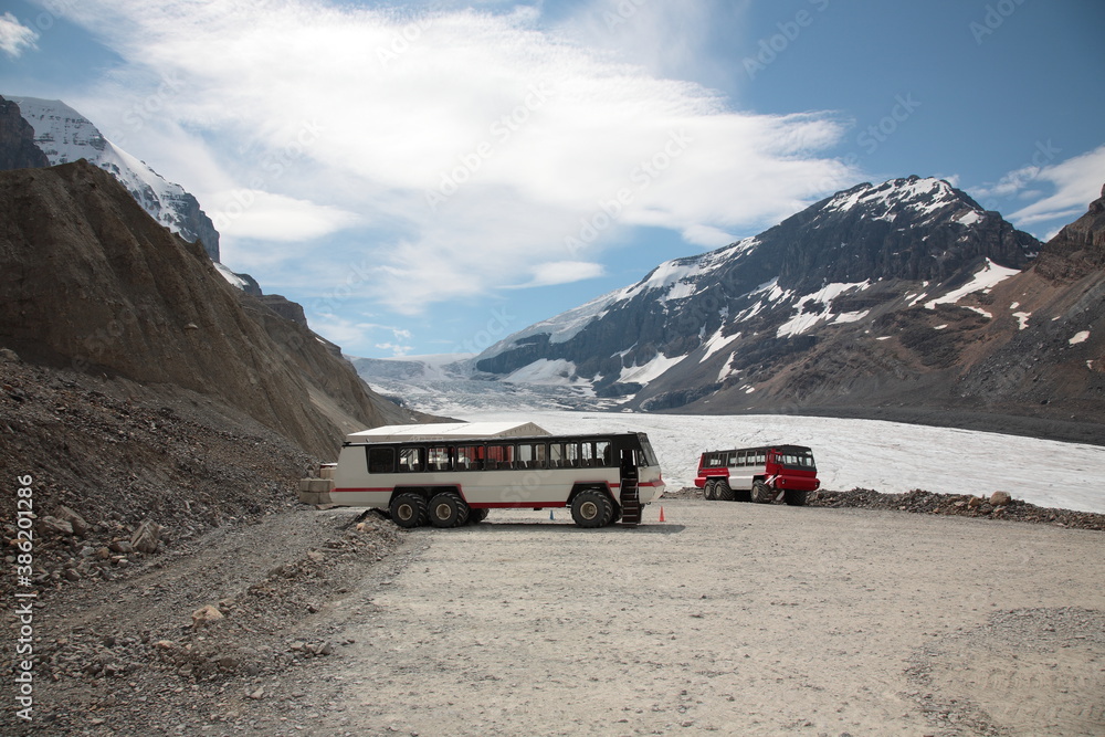 View of Athabasca Glacier with snow mountain peaks and Ice Explorer massive vehicle snow coach bus during summer  in the boundary of Banff and Jasper National Park, Canadian Rockies, Alberta, Canada.
