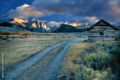In the light of evening dirt road and cabin with mountains