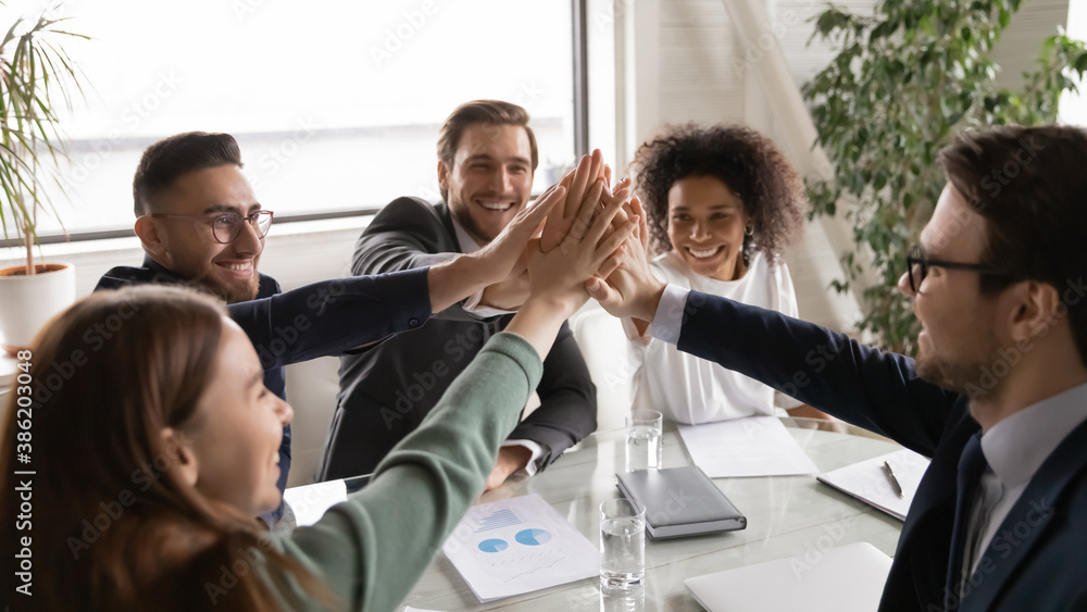 Positive happy young multiracial diverse colleagues giving high five, celebrating group business achievement, company growth or financial marketing strategy results at brainstorming meeting in office. Positive happy young multiracial diverse colleagues giving high five, celebrating group business achievement, company growth or financial marketing strategy results at brainstorming meeting in office.