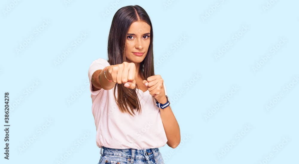 Young hispanic woman wearing casual white tshirt punching fist to fight, aggressive and angry attack, threat and violence Young hispanic woman wearing casual white tshirt punching fist to fight, aggressive and angry attack, threat and violence