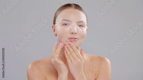 Beauty Portrait Of Young Caucasian Blonde Woman With Blue Eyes She Applying Finger White Paper Tissue Sheet Mask On Face On Gray Background Skin Care Concept Slow Motion