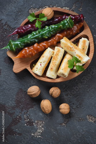 Wooden serving tray with traditional georgian churchkhelas and fried crepes, above view on a brown stone background, vertical shot with space photo