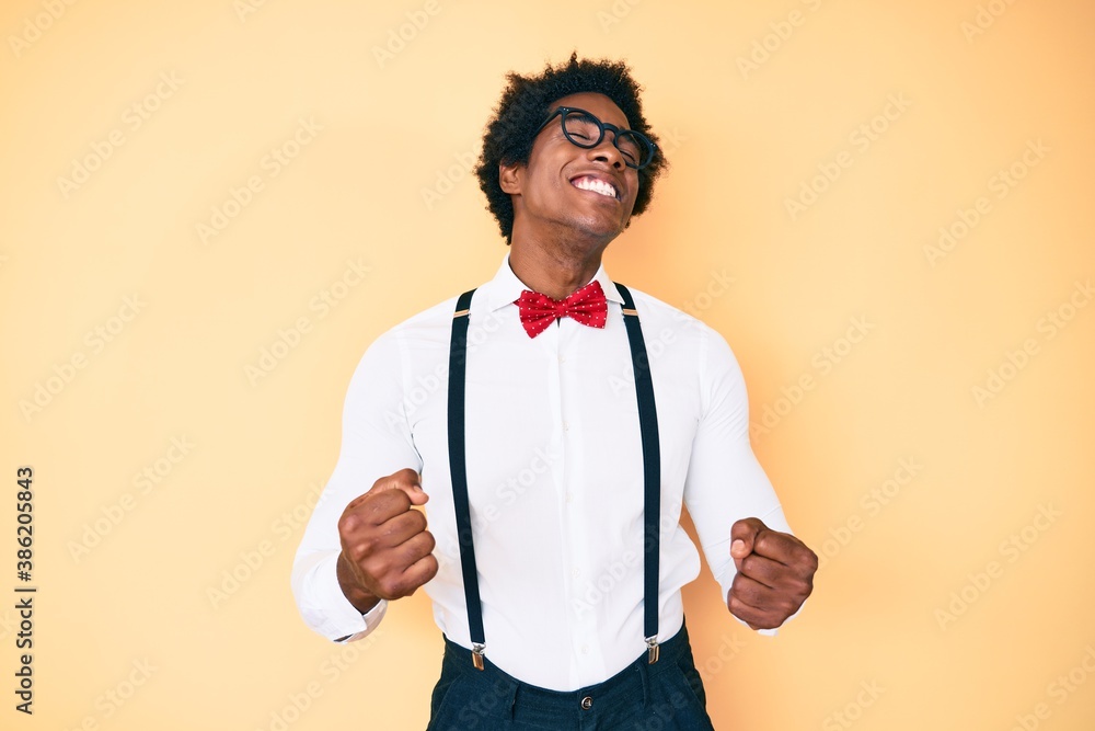 Handsome african american man with afro hair wearing hipster elegant look very happy and excited doing winner gesture with arms raised, smiling and screaming for success. celebration concept. Handsome african american man with afro hair wearing hipster elegant look very happy and excited doing winner gesture with arms raised, smiling and screaming for success. celebration concept.