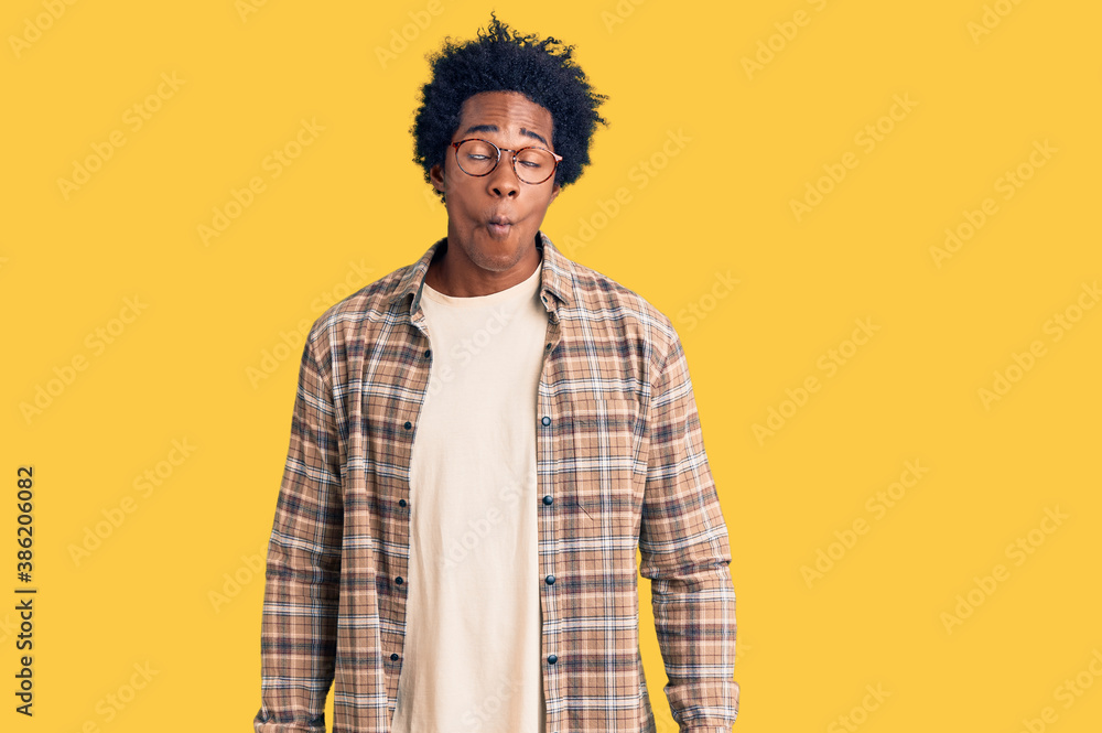 Handsome african american man with afro hair wearing casual clothes and glasses making fish face with lips, crazy and comical gesture. funny expression. Handsome african american man with afro hair wearing casual clothes and glasses making fish face with lips, crazy and comical gesture. funny expression.