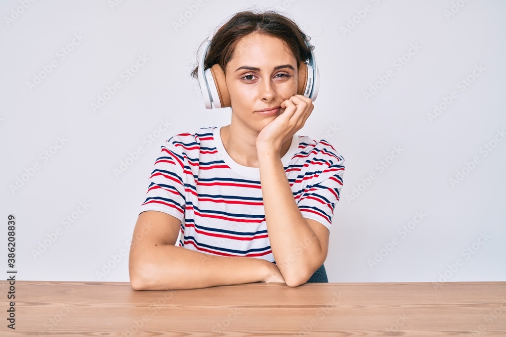 Young hispanic woman using headphones sitting on the table thinking looking tired and bored with depression problems with crossed arms. Young hispanic woman using headphones sitting on the table thinking looking tired and bored with depression problems with crossed arms.