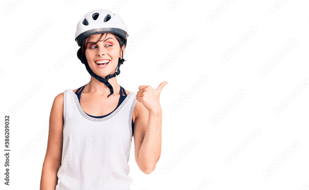 Beautiful young woman with short hair wearing bike helmet smiling with happy face looking and pointing to the side with thumb up. Beautiful young woman with short hair wearing bike helmet smiling with happy face looking and pointing to the side with thumb up.