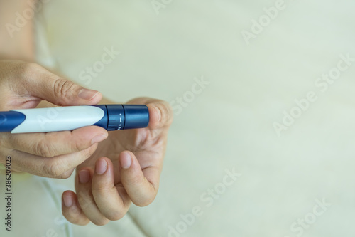 Close up of woman hands using lancet on finger to check blood sugar level by Glucose meter. Use as Medicine, diabetes, glycemia, health care and people concept.