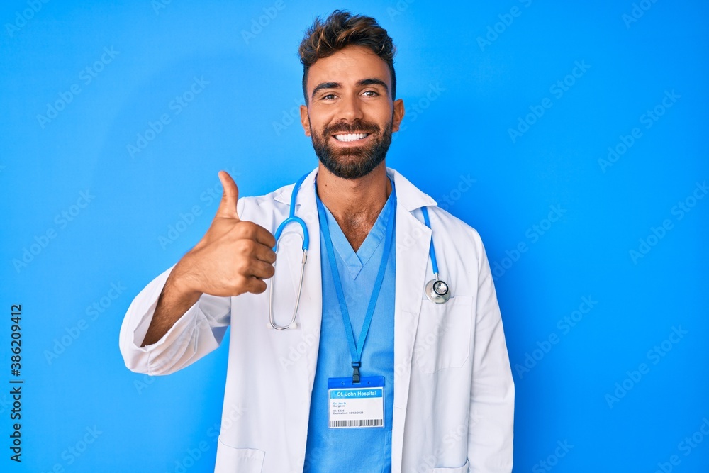 Young hispanic man wearing doctor uniform and stethoscope smiling happy and positive, thumb up doing excellent and approval sign Young hispanic man wearing doctor uniform and stethoscope smiling happy and positive, thumb up doing excellent and approval sign