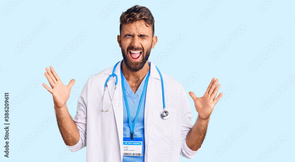 Young hispanic man wearing doctor uniform and stethoscope celebrating mad and crazy for success with arms raised and closed eyes screaming excited. winner concept