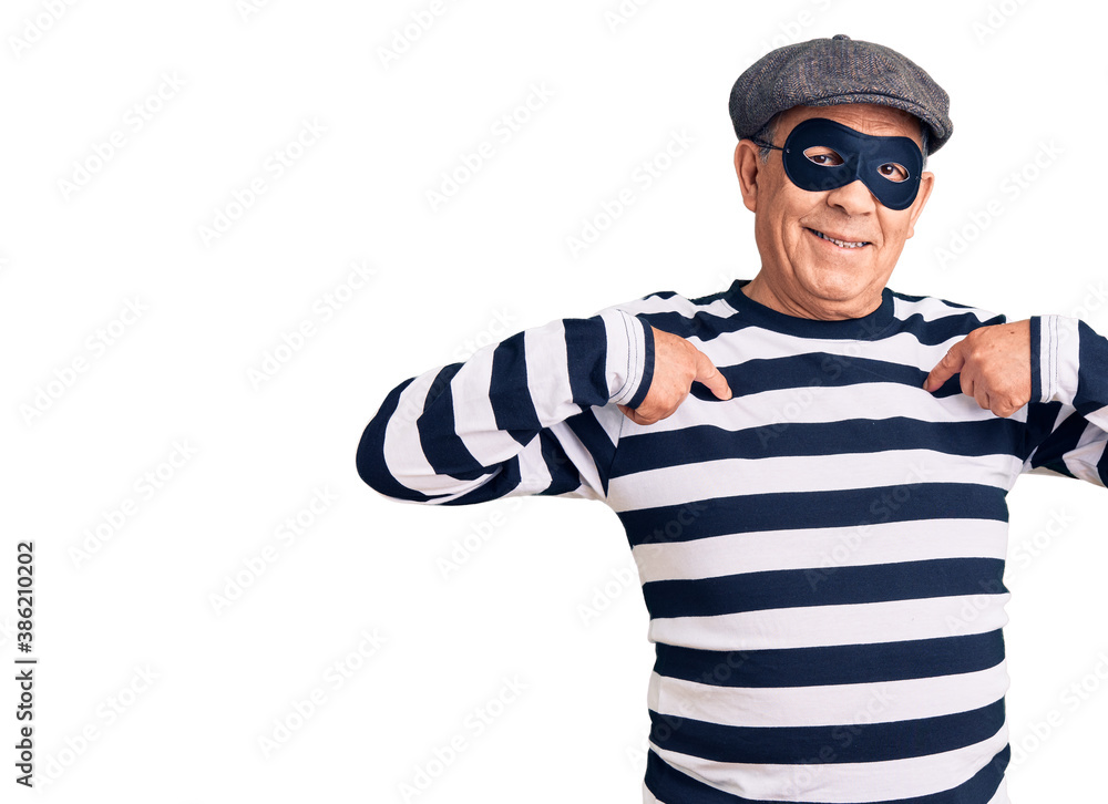 Senior handsome man wearing burglar mask and t-shirt looking confident with smile on face, pointing oneself with fingers proud and happy. Senior handsome man wearing burglar mask and t-shirt looking confident with smile on face, pointing oneself with fingers proud and happy.