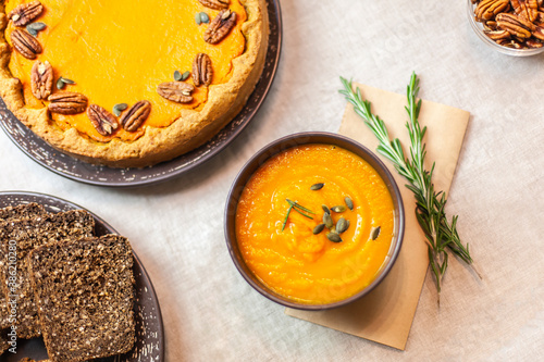 Autumn party, pumpkin dinner: orange soup, pumpkin pie decorated with pecans on a served table and other dishes