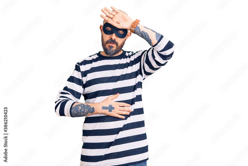 Young handsome man wearing burglar mask touching forehead for illness and fever, flu and cold, virus sick Young handsome man wearing burglar mask touching forehead for illness and fever, flu and cold, virus sick