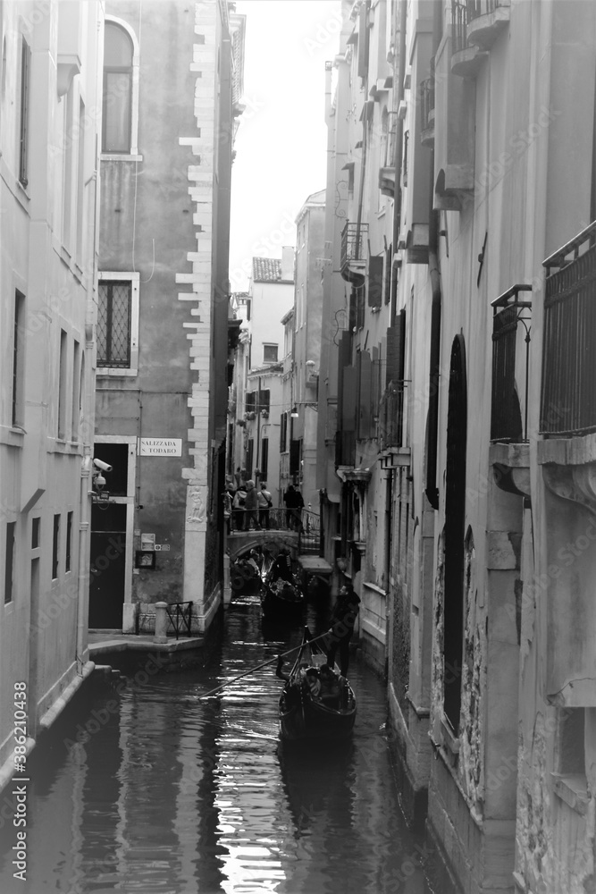 Venice, Italy, December 28, 2018 evocative black and white image of a narrow passage for the 
calle of Venice with a gondola passing in the background
