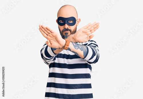 Young handsome man wearing burglar mask rejection expression crossing arms and palms doing negative sign, angry face © Krakenimages.com