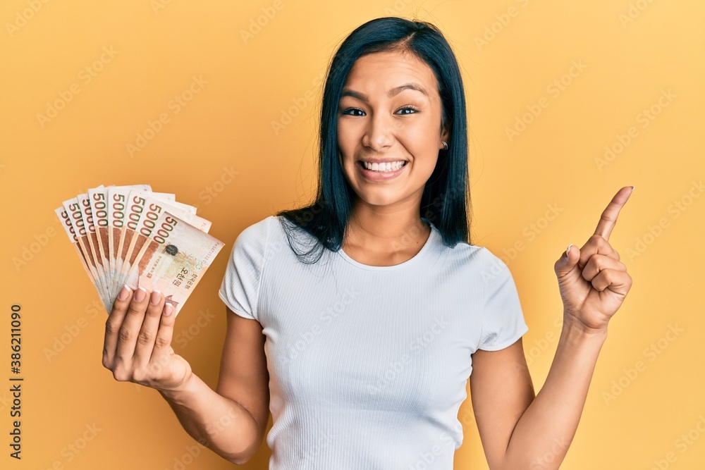 Beautiful hispanic woman holding 5000 south korean won banknotes smiling happy pointing with hand and finger to the side Beautiful hispanic woman holding 5000 south korean won banknotes smiling happy pointing with hand and finger to the side