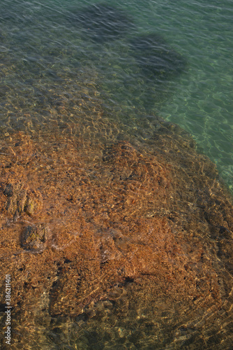 turquoise Mediterranean sea detail during summer with rocks, waves, and sunlight vertical