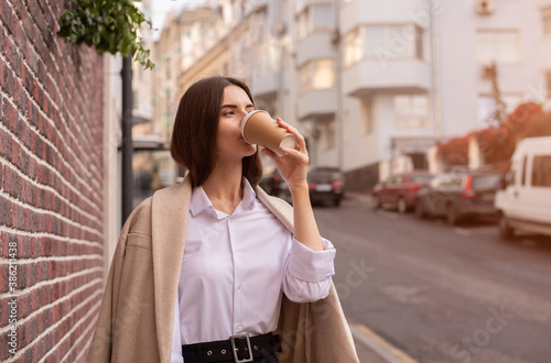 A young woman walks down the street. Drink your morning coffee. © Anastasiia