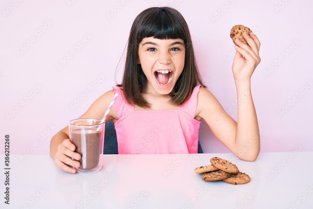 Young little girl with bang sitting on the table having breakfast celebrating crazy and amazed for success with open eyes screaming excited. Young little girl with bang sitting on the table having breakfast celebrating crazy and amazed for success with open eyes screaming excited.