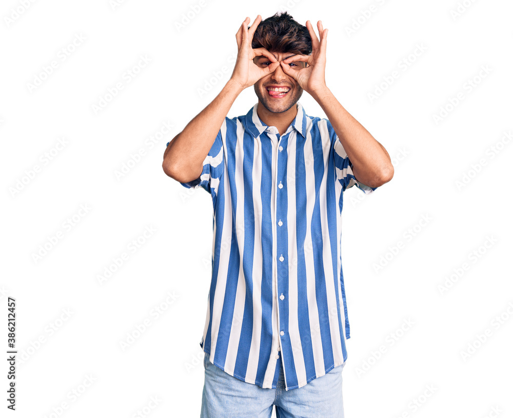 Young hispanic man wearing casual clothes doing ok gesture like binoculars sticking tongue out, eyes looking through fingers. crazy expression. Young hispanic man wearing casual clothes doing ok gesture like binoculars sticking tongue out, eyes looking through fingers. crazy expression.